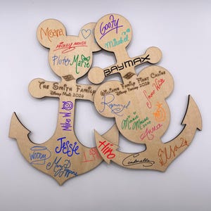 May include: Wooden anchor-shaped sign with Mickey Mouse ears, featuring signatures and names like "Moana," "Goofy," and "Baymax." The sign includes the text "The Smith Family Disney Music 2020" and "Williams Family First Cruise Disney Fantasy 2026."