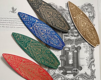 May include: Five wooden bookmarks with intricate patterns in various colors, including black, blue, green, and red. The bookmarks are shaped like surfboard fins and have a decorative design.