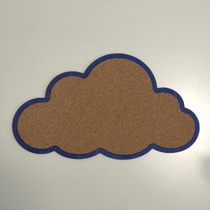 May include: A cloud-shaped cork board featuring a textured brown cork surface framed by a solid dark blue border. The object has a distinct rounded, scalloped outline that mimics the appearance of a stylized cloud, providing a flat surface.