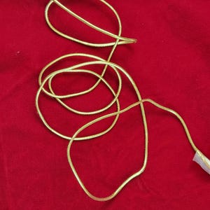May include: A gold-colored chain necklace, coiled on a red background. The chain has a textured, snake-like design. The necklace is shown in a close-up shot, highlighting its details and shine.