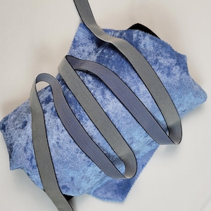 May include: A roll of gray elastic ribbon with a black edge, on a blue velvet fabric.