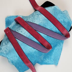 Pode incluir: Duas fitas de veludo, uma rosa e outra roxa, são enroladas em torno de um pedaço de tecido de veludo azul.