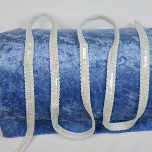 May include: White iridescent sequin trim ribbon on a blue velvet background.