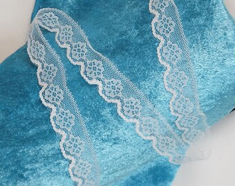 May include: Two pieces of white lace trim on a blue velvet background. The lace has a scalloped edge and a delicate floral pattern.