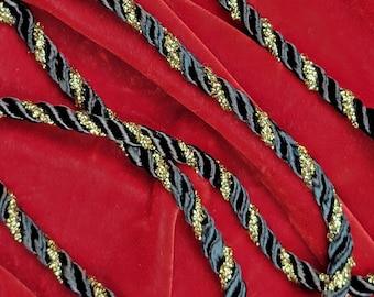 May include: Black and gold twisted rope trim with a sparkly finish. The trim is shown on a red velvet background.