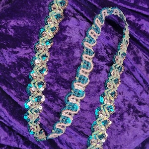 Può includere: Bordino di paillettes turchesi e argento con bordo smerlato. Il bordino è su uno sfondo di velluto viola.