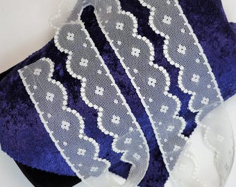 May include: White lace trim with a scalloped edge and small flower pattern. The trim is shown on a dark blue velvet background.