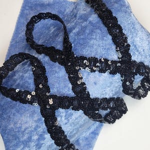 Peut inclure: Un tissu en velours bleu avec une bordure en sequins noirs. La bordure est pliée et torsadée, créant un motif décoratif.
