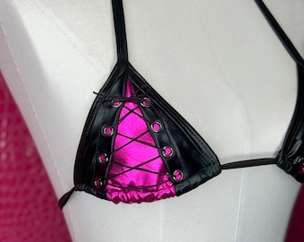 Può includere: Top bikini nero e rosa con design allacciato. Le coppe triangolari sono nere con occhielli argentati e un centro rosa acceso. Le spalline e il laccio posteriore sono neri.