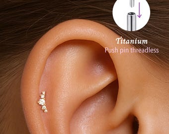 May include: Close-up of a gold-colored ear piercing with multiple clear, round gemstones. The piercing is set against the skin of an ear. The text "Titanium Push pin threadless" is visible.