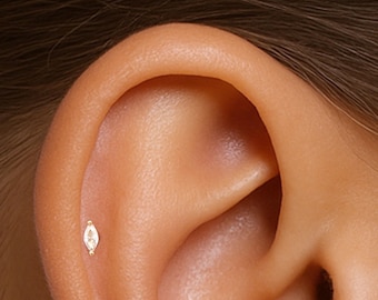 May include: A close-up of a person's ear with a small, gold, marquise-shaped stud earring with a clear stone.