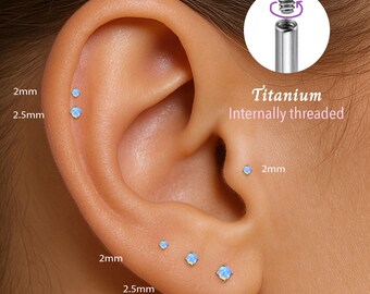 May include: Close-up of an ear with multiple titanium internally threaded earrings with small blue opal stones. The earrings are available in 2mm, 2.5mm, and 3mm sizes.