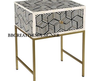 Könnte beinhalten: Ein Beistelltisch mit geometrischem Muster in Schwarz und Weiß, einer Schublade und goldenen Metallbeinen. Die Schublade hat einen goldenen Knopf. Der Tisch ist aus Knocheninlay gefertigt.
