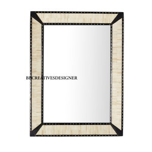 May include: A rectangular mirror with a black frame and a white bone inlay design. The frame is decorated with black dots.
