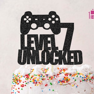 May include: Black glitter cake topper with a video game controller and the text "Level 7 Unlocked".