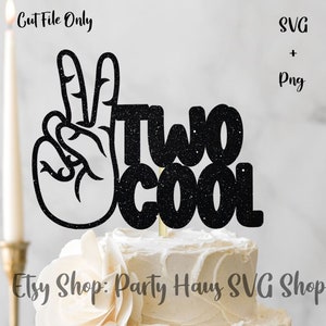 Może przedstawiać: Czarny topper na ciasto z brokatem z napisem "Two Cool" i znakiem pokoju. Topper znajduje się na białym cieście z białym kremem.