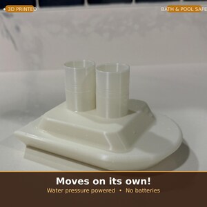 May include: A 3D-printed, off-white toy boat with two cylindrical smokestacks. The boat is designed to move on its own using water pressure, with no batteries required. The text "BATH & POOL SAFE" is visible.