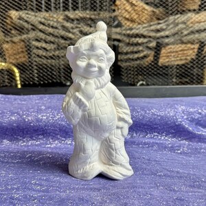 May include: White ceramic gnome figurine with a textured surface and a smiling face. The gnome is wearing a hat and has a beard.
