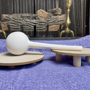 May include: White ceramic bulb with a long, thin neck resting on a wooden base. The bulb is on a purple surface.