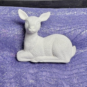 May include: A white ceramic deer figurine in a lying down position. The deer has a detailed face and fur texture.