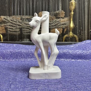 May include: White ceramic deer figurine with a simple design. The deer is standing on a square base.