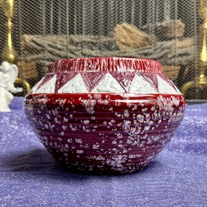 May include: A red and white ceramic planter with a geometric design. The planter has a speckled glaze and a rounded shape.