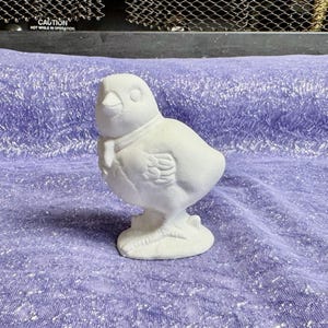 May include: White ceramic figurine of a bird with a bow tie. The bird is standing on a base and has a round body and a small beak.