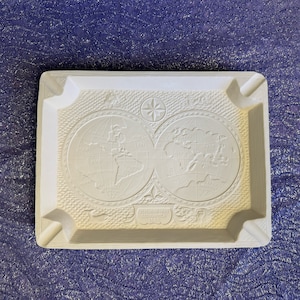 May include: White ceramic ashtray with a raised design of two globes and a compass. The globes are labeled with continents and oceans. The text "TERRAQUEA GEOGRAPHICA 1530" is at the bottom.