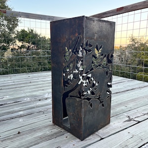 May include: A rusty metal planter with a tree design cut out. The planter is on a wooden deck.