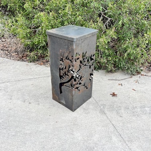 May include: A rusty metal planter with a tree design cut out. The planter is square and has a flat top.