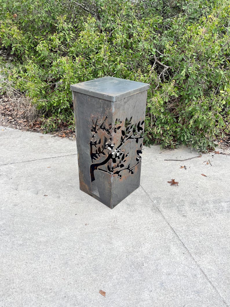 May include: A rusty metal planter with a tree design cut out. The planter is square and has a flat top.