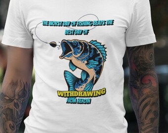 Puede incluir: Camiseta blanca con un gráfico de pez azul y beige y el texto "THE WORST DAY OF FISHING BEATS THE BEST DAY OF WITHDRAWING FROM HEROIN". El diseño incluye un anzuelo.