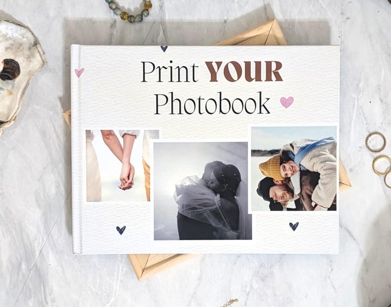 May include: A white photobook with the text "Print YOUR Photobook" and three photo inserts. The cover is decorated with small pink and black hearts. The photos show couples in various settings.