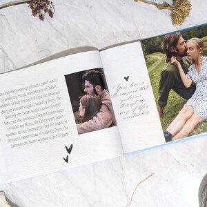 May include: Open photo album with a light blue cover, featuring photos of a couple and handwritten text. The text includes phrases like "sweetest dream" and "live forever." A bracelet and dried flowers are visible.