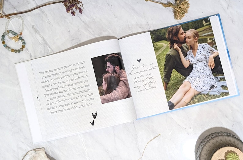 May include: Open photo album with a light blue cover, featuring photos of a couple and handwritten text. The text includes phrases like "sweetest dream" and "live forever." A bracelet and dried flowers are visible.