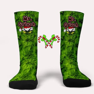 以下が含まれることがあります： 緑色のグリンチをテーマにした靴下で、各靴下に「Mr. Grinch」の文字が書かれています。靴下は緑色のふわふわした質感で、グリンチの顔の漫画が描かれています。