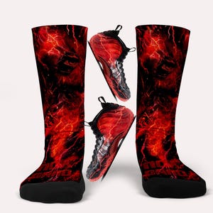 May include: A pair of knee-high socks and two sneakers. The socks and sneakers have a red and black design with a fiery, lightning-like pattern. The socks have a black toe and heel.