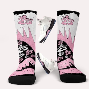Peut inclure: Des chaussettes montantes noires, roses et blanches avec le numéro 23 et un motif en zigzag. Deux baskets blanches et roses sont également présentes dans l'image.
