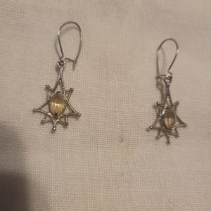 May include: A pair of silver dangle earrings with a star-shaped design and a clear yellow gemstone in the center.