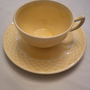 May include: A yellow teacup and saucer set. The saucer has a woven pattern.