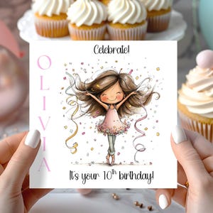 May include: A birthday card held by a person, featuring a cartoon girl with outstretched arms, confetti, and the text "Celebrate!" and "It's your 10th birthday!" The name "Olivia" is printed vertically on the left side of the card in pink.