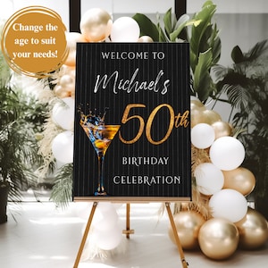May include: Black and gold welcome sign with white pinstripes. The sign says "Welcome to Michael's 50th Birthday Celebration". A martini glass with a gold rim is in the corner of the sign.