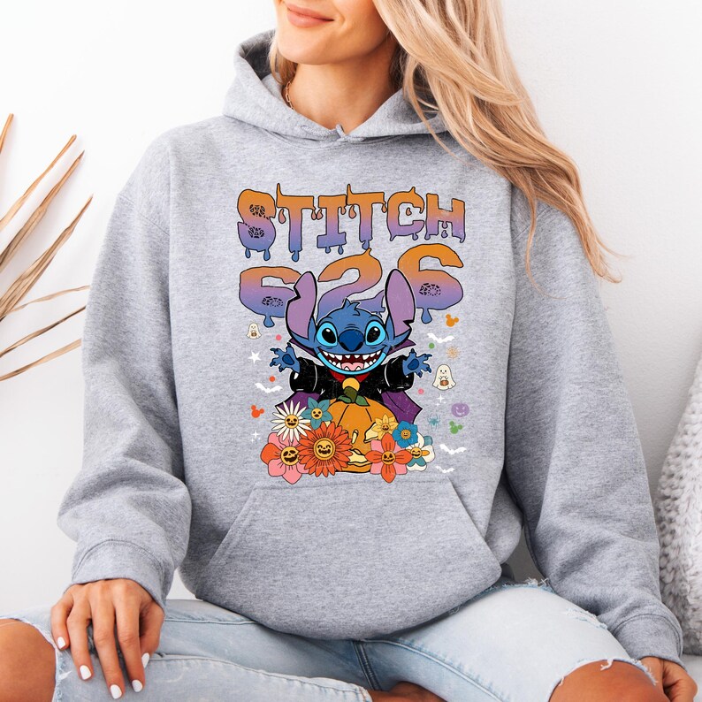 May include: A light gray hoodie featuring a graphic of Stitch from Lilo & Stitch dressed as a vampire, with the text "Stitch 626". The design includes a pumpkin, flowers, and Halloween-themed elements.