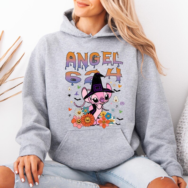 May include: A light gray hoodie featuring a graphic of a pink alien character wearing a witch hat, surrounded by flowers and bats. The text "ANGEL 624" is printed above the character in orange and purple. The hoodie has a drawstring hood.