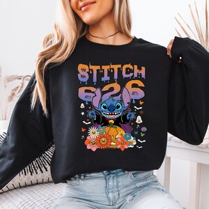 May include: Black sweatshirt featuring a colorful graphic of Stitch from Lilo & Stitch, with the text "Stitch 626". The design includes a pumpkin, flowers, and Halloween-themed elements.