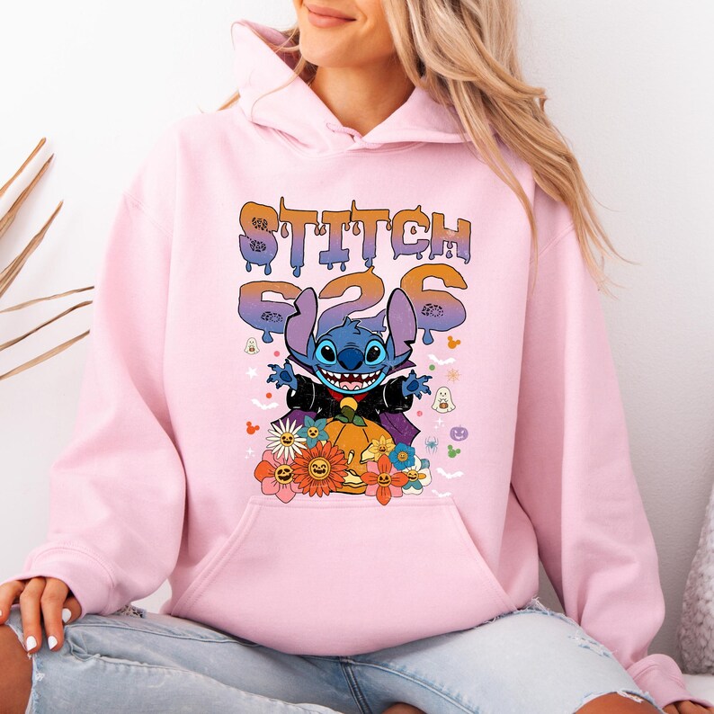 May include: A light pink hoodie featuring a graphic of Stitch from Lilo & Stitch. The graphic includes the text "STITCH 626" in a dripping font, Stitch in a Halloween costume, a pumpkin, and flowers.