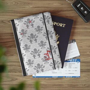 May include: A passport holder with a white and gray floral pattern and the name "Kathy" written in red. The holder is next to a passport and two airline boarding passes.