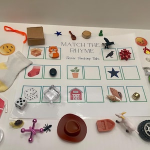 May include: A set of rhyming matching game cards with a variety of colorful images, including a red barn, a green car, a red bow, a brown cowboy hat, a white sock, a green plant, a black crow, a white star, a brown seashell, a red fox, a brown dice, a clear glass container, and a gold bell. The cards are labeled "Match the Rhyme" and "Tinkler Teaching Tubs".