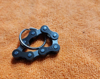 May include: A silver key chain with a black bike chain design. The chain has the word "BELL" printed on it.