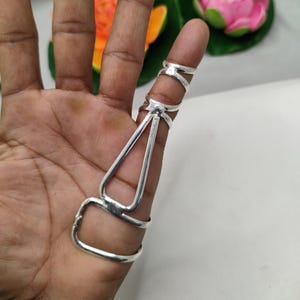 Op de afbeelding: Een zilveren vingerringset. De set bevat een ring voor de basis van de vinger, een ring voor het midden van de vinger en een ring voor de vingertop, verbonden door een decoratief ontwerp.